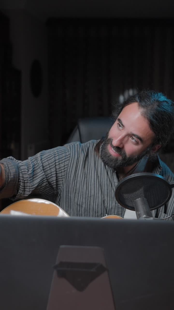 Man playing guitar and recording music with microphone and smartphone in a studio