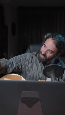 man playing guitar and recording music with microphone and smartphone in a studio