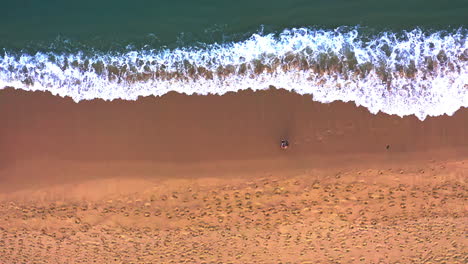 Woman-walking-on-sandy-beach-washed-by-foamy-ocean-waves-in-Thailand