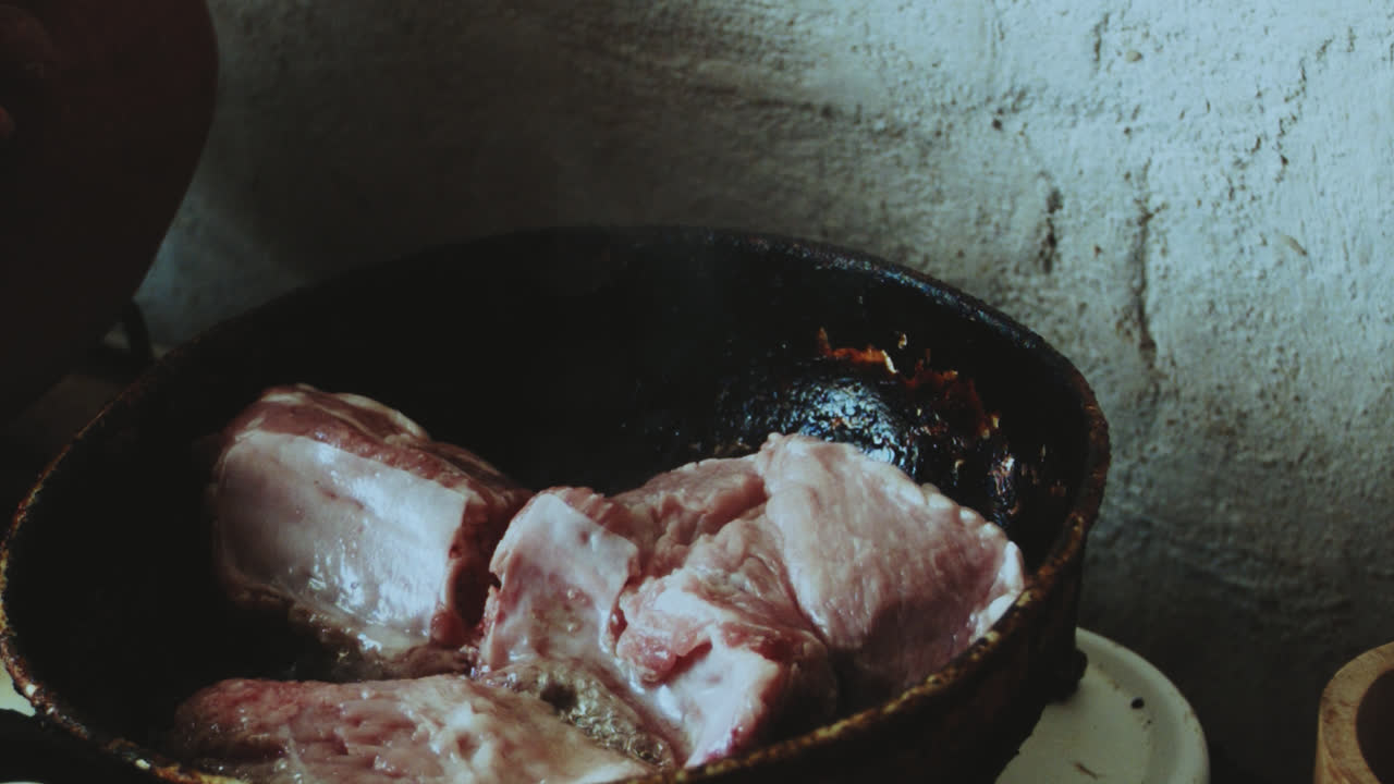 Beautiful close-up shot of an older Latin woman cooking pork prey with oil in a frying pan inside a rustic stone kitchen in a humble village house in Peru.