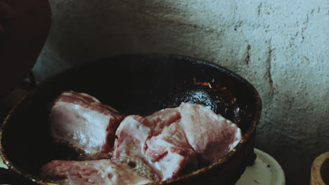 beautiful close-up shot of an older latin woman cooking pork prey with oil in a frying pan inside a rustic stone kitchen in a humble village house in peru.
