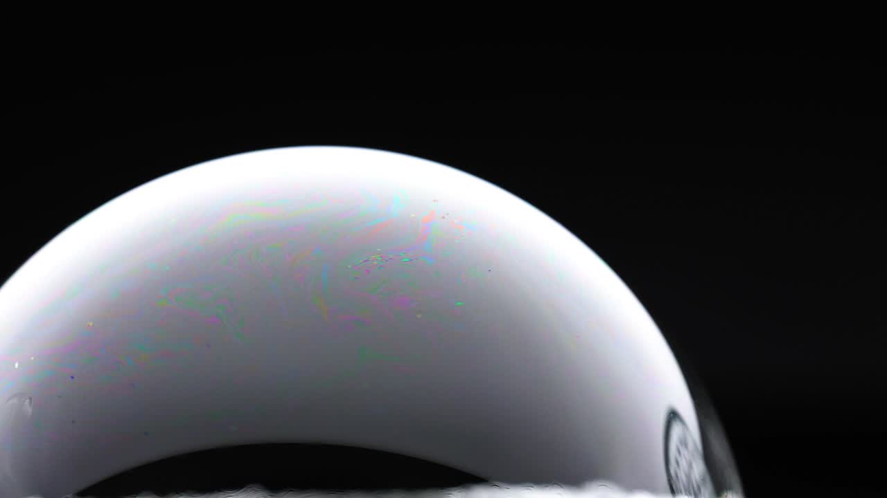 A soap bubble displays vibrant color reflections against a dark background, highlighting optical phenomena and delicate surface patterns