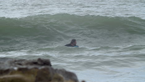 Sportive-Man-In-Wetsuit-With-Artificial-Leg-Lying-On-Surfboard-And-Swimming-In-The-Ocean-When-A-Wave-Covering-Him