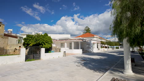 a traditional house with a red-tiled roof and white walls in pafos, set against a bright blue sky. the house is surrounded by a clean, paved area and greenery, creating a peaceful atmosphere