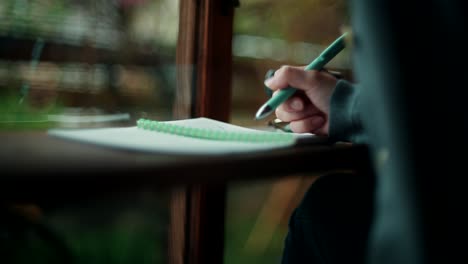 person writing in a notebook by a window