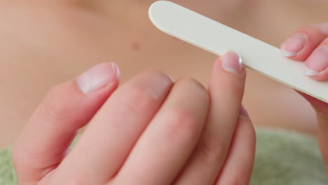 close up hand view of woman filing and shaping fingernails using white filer, focusing on clean nail edges and personal grooming process, representing home selfcare and beauty treatment indoors