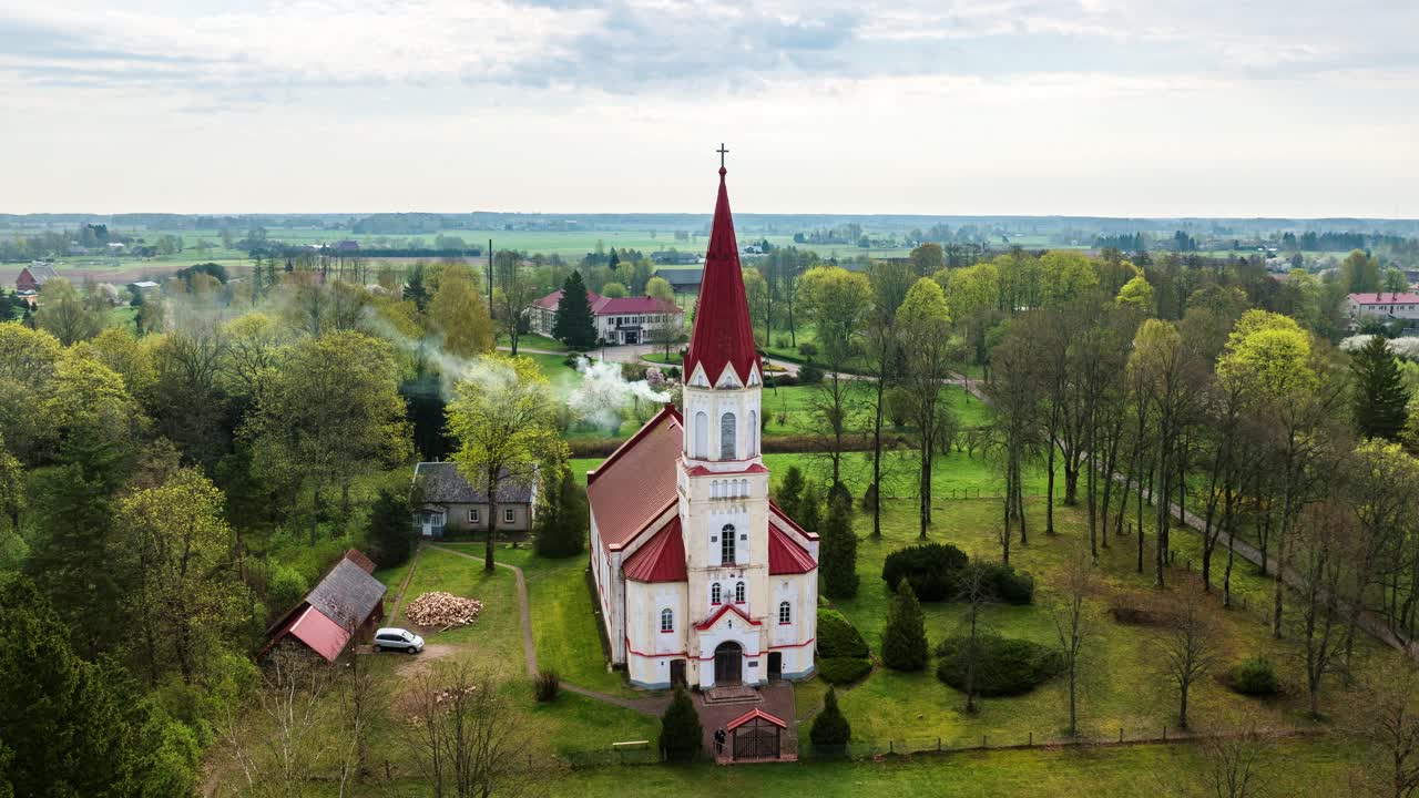 Full 360 hyperlapse shows Rucava Lutheran Church with red roof, chimney smoke
