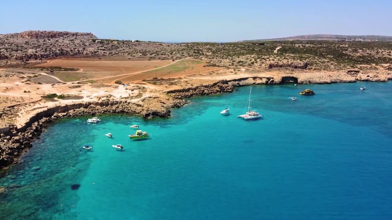 Vista aerea di barche ancorate in acque turchesi cristalline vicino a una costa frastagliata e assolata