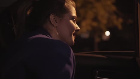 Close-Up-view-of-happy-beautiful-girl-riding-in-a-taxi-at-night-sitting-on-the-backseat-and-looking-in-the-camera-and-after-that