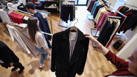 people shopping for clothes and trying on a black jacket in a clothing store