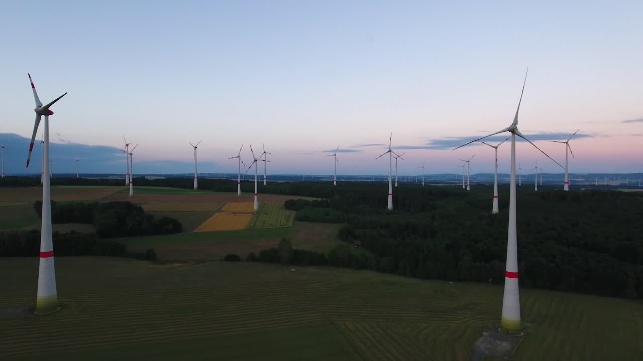 Drone aerial flying forward towards wind turbine farm in a large open field