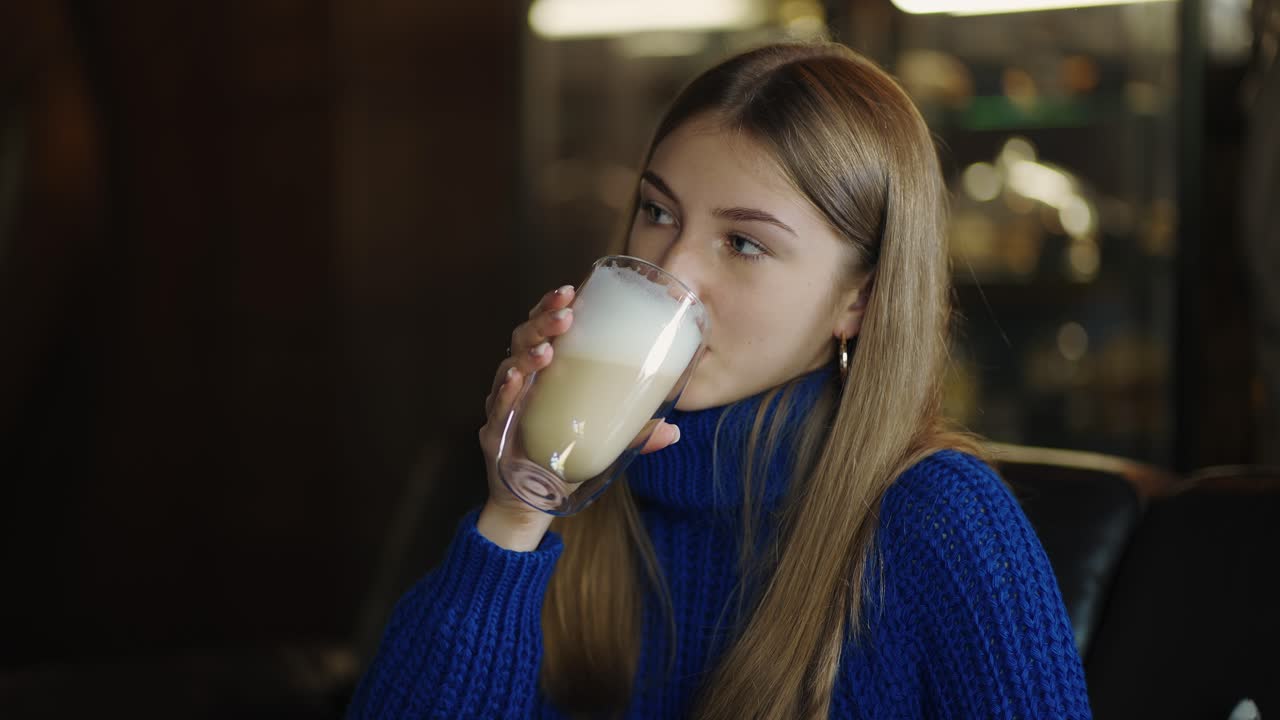mujer sonriente sostiene una gran taza transparente de capuchino en las manos y luego bebe