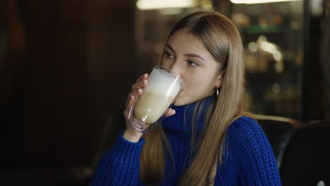 smiling woman holds big transparent cup of cappuccino in hands then drinks