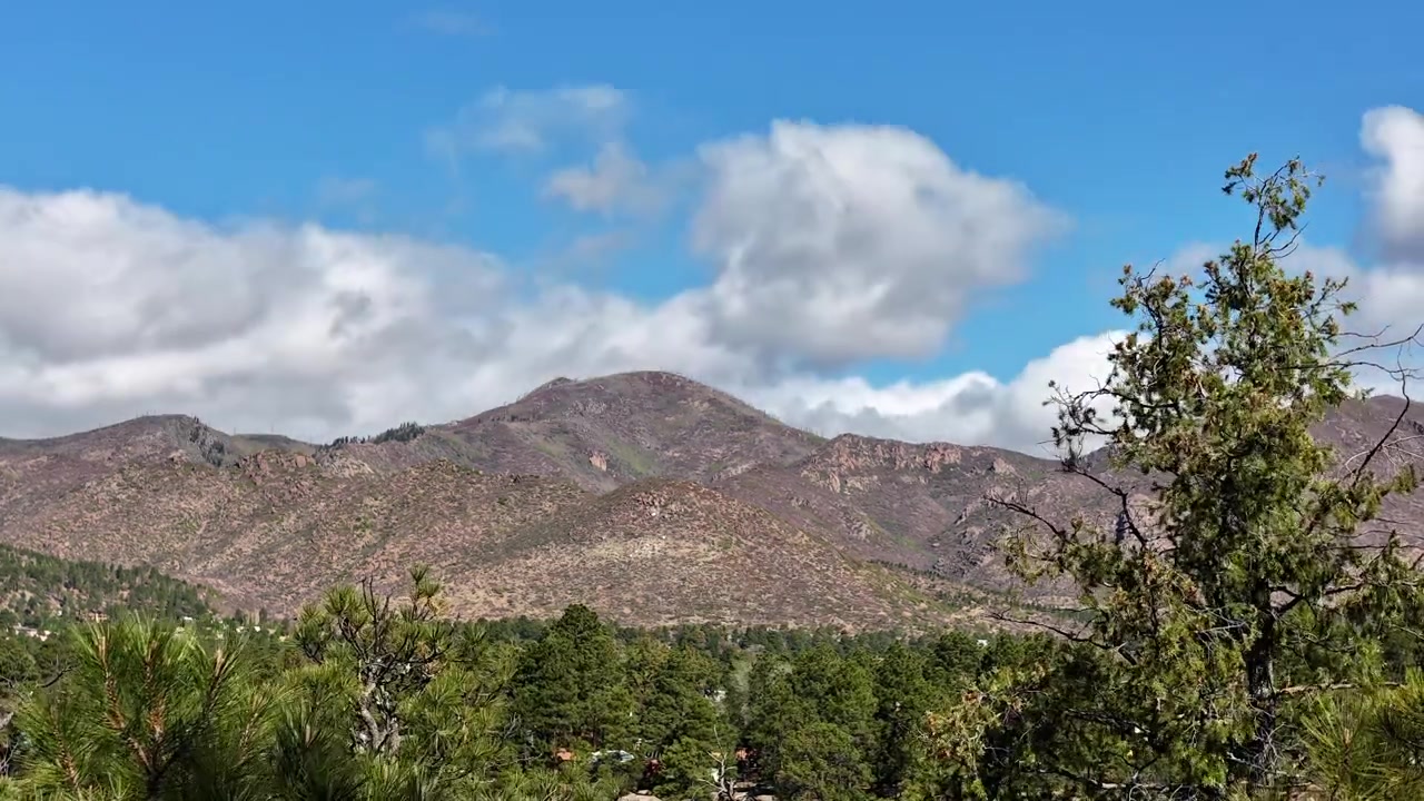 Timelapse 4K cattura nuvole in rapido movimento sopra una cima montuosa aspra, al di sopra di una fitta foresta di pini. Il movimento atmosferico cinematografico rivela nuvole bianche che si spostano su una vasta veduta di natura selvaggia ad alta quota.