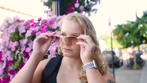 Girl-puts-on-aviator-sunglasses-outside-in-front-of-flowers-in-the-city