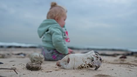 Nahaufnahme-Einer-Plastikflasche-Am-Strand-Mit-Einem-Kleinen-Mädchen-Dahinter-Sitzend