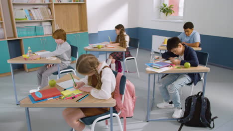 over the shoulder shot of an unrecognizable male teacher looking his pupils who writing in their notebook during english class at school