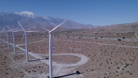 drone rotates around a windmill, revealing a line of working windmills in the desert