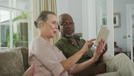 happy senior diverse couple wearing shirts and using tablet in living room
