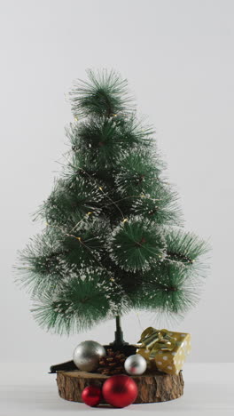 disparo vertical de un pequeño árbol de navidad en un soporte de madera sobre un fondo blanco