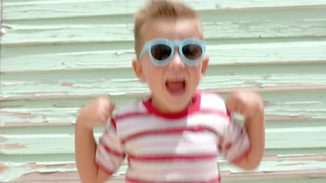 portrait of happy caucasian boy with sunglasses raising hands over beach house