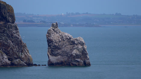 a lone cliff rises from the waters off howth peninsula, standing tall against the waves. the rugged coastline and deep blue sea showcase the raw beauty of ireland’s eastern shore.