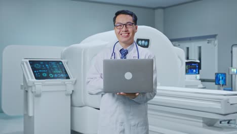 asian male doctor holding a laptop and smiling with mri machine in the hospital