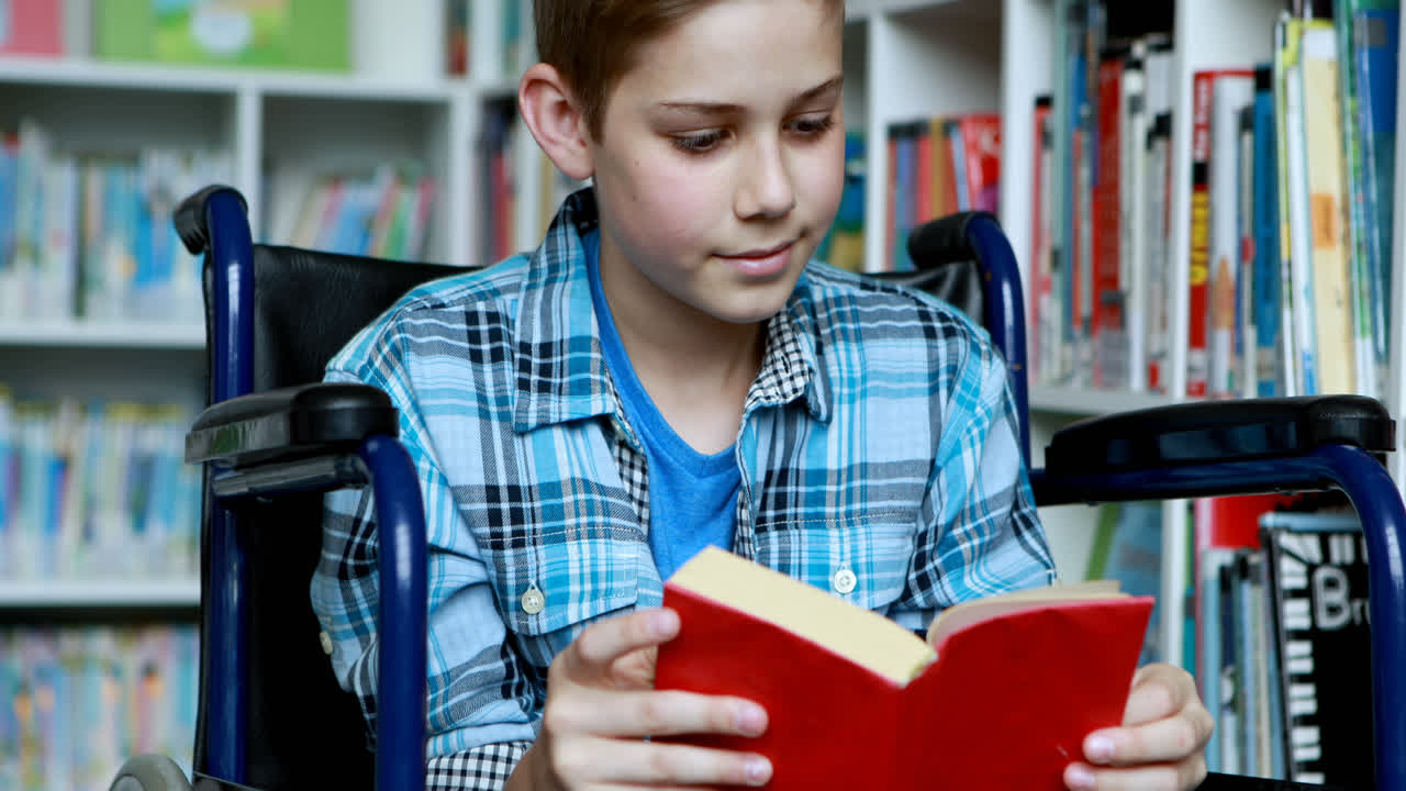 Disabled schoolboy on wheelchair reading book in library