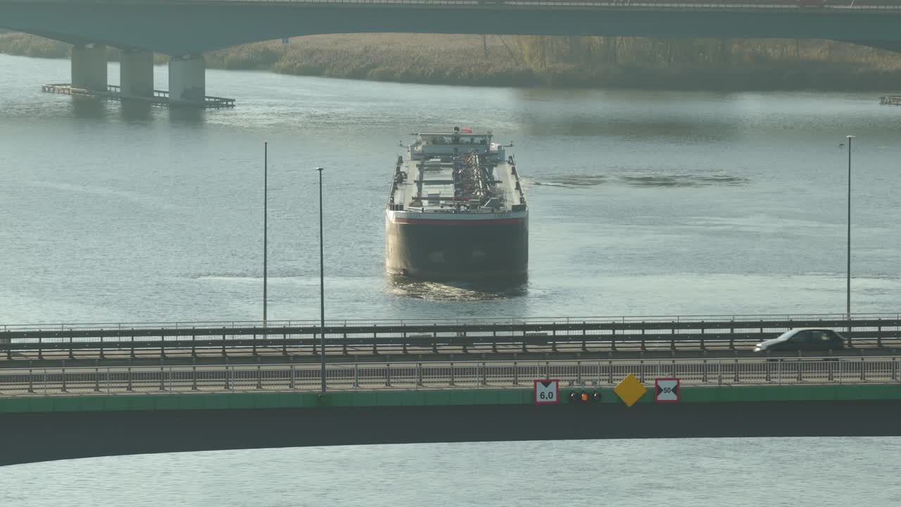 原油油輪在平靜河流上的橋下駛近工業港口，推動全球能源貿易。