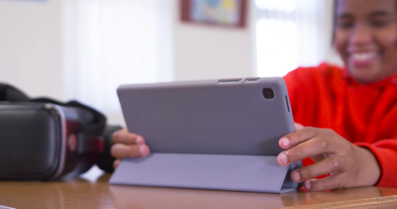 Adolescente afroamericano che guarda il tablet, toccando e ruotando per cambiare angolazione al tavolo con visore VR