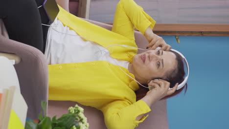 vertical video of woman looking out the window and listening to music with headphones.