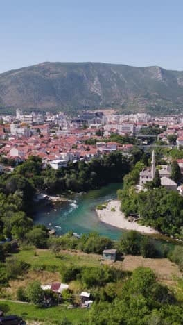 panoramic vertical drone view of mostar with river, red rooftops and green mountain backdrop