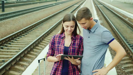 un hombre y una mujer atractivos están en la estación de tren usan la tableta
