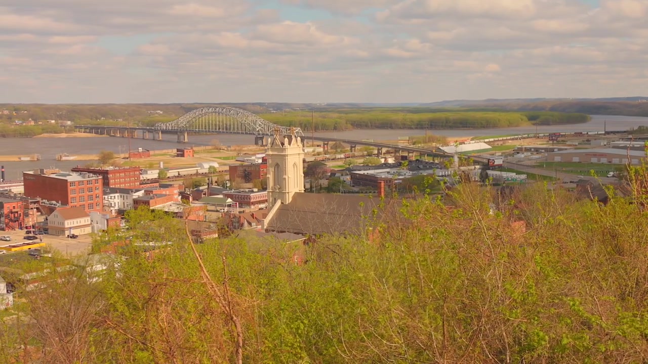 Amplia vista panorámica de Dubuque, Iowa, con vistas a la ciudad, el histórico campanario de la catedral y el majestuoso río Misisipi con un puente al fondo.