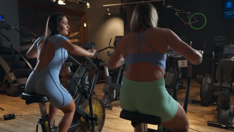 blond and brown caucasian women from behind doing elliptical at the gym, indoor, medium shot
