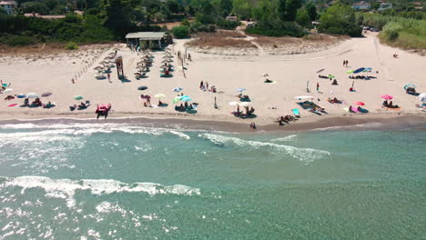 idyllic beach with tourists, sunbeds and umbrellas on a sunny day of summer in sardinia, italy - aerial sideways