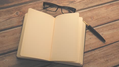 open notebook with pen and glasses on wooden table