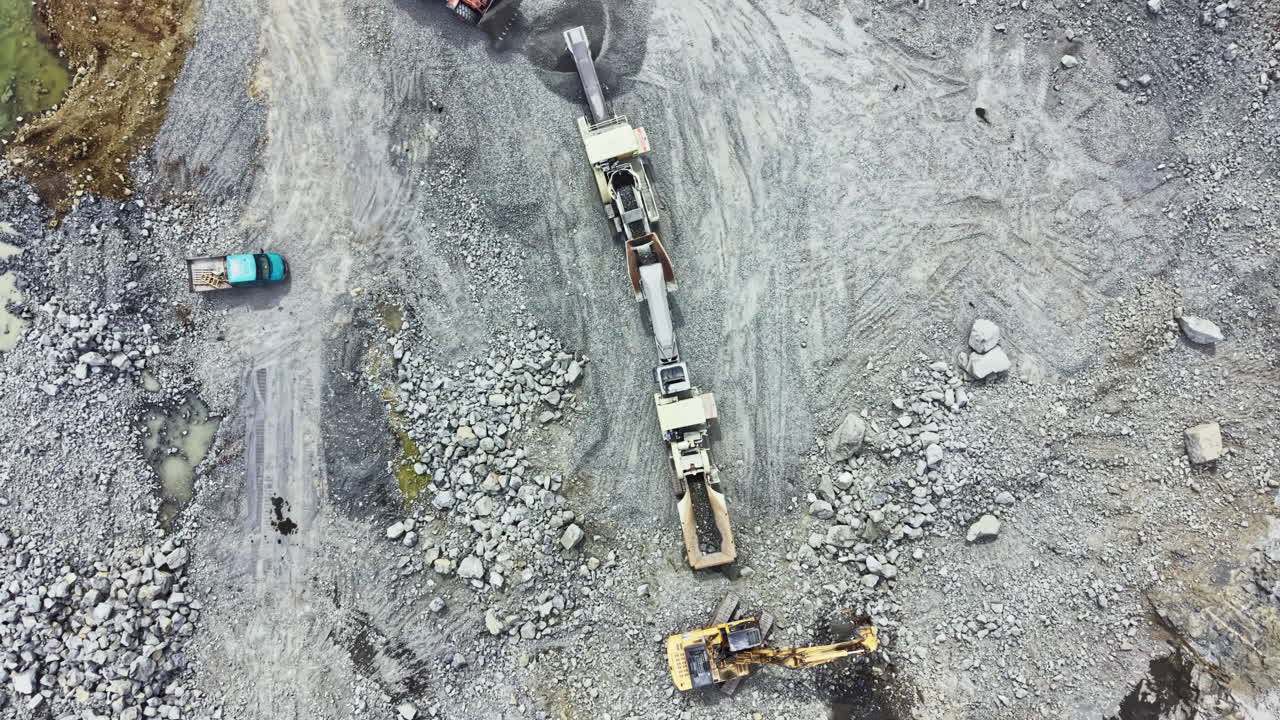 Granitbrud i drift i dagslys med tungt maskineri, der udvinder sten, og lastbiler, der transporterer materialer