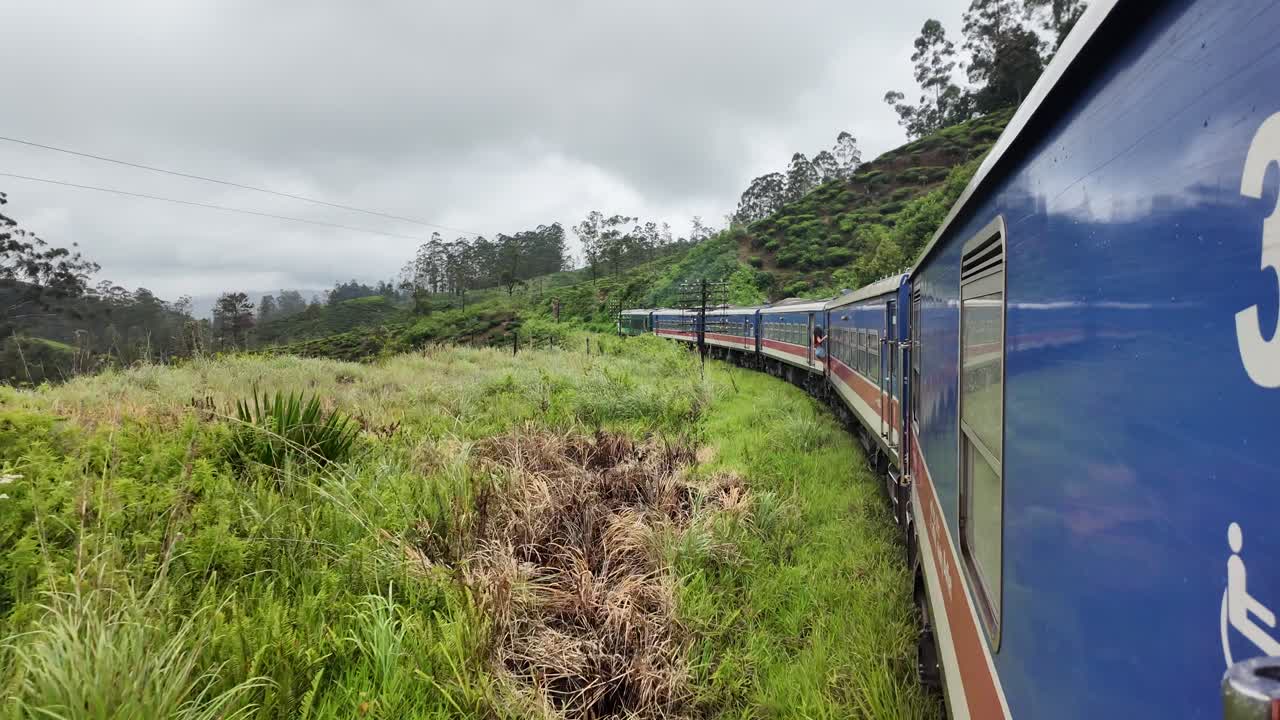 Train travels through the lush, green hills of Bandarawela, Sri Lanka, surrounded by dense foliage and misty landscape. slow motion
