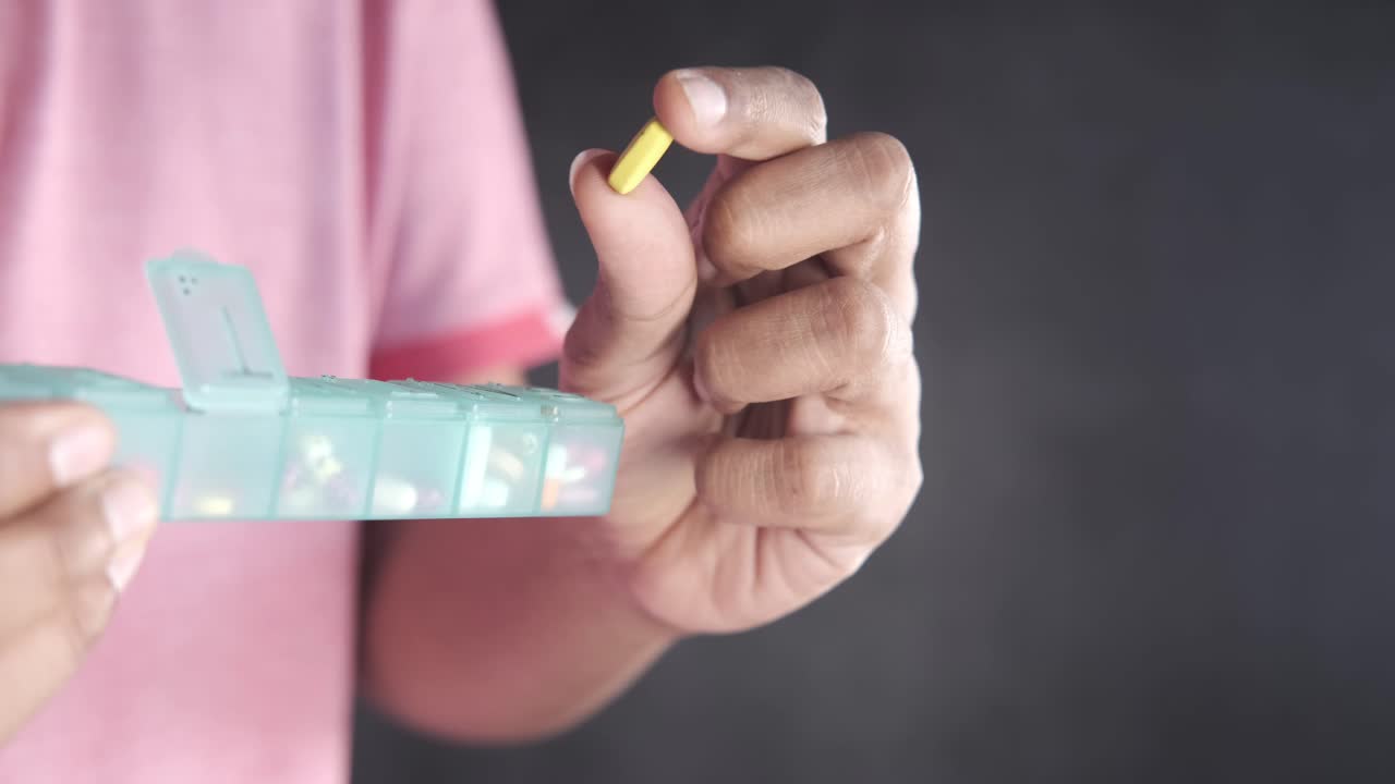 persona que sostiene una píldora y un organizador de píldoras
