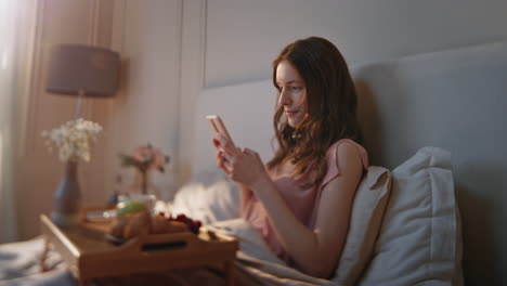 beautiful model using mobile phone in cozy bedroom closeup. serene morning girl