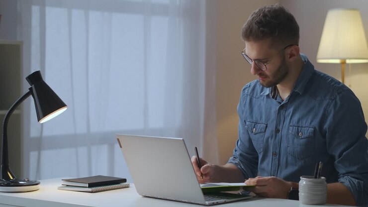 Voksen mand lytter til en samtalepartner via videoopkald på en bærbar computer og tager noter under et online forretningsmøde i isolationsperioden og pandemien.
