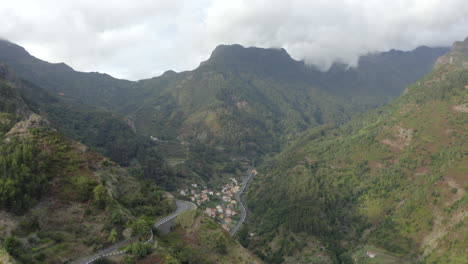 sinuoso paso de montaña con vistas a una pequeña ciudad en las estribaciones de una montaña verde en la isla de madeira, portugal
