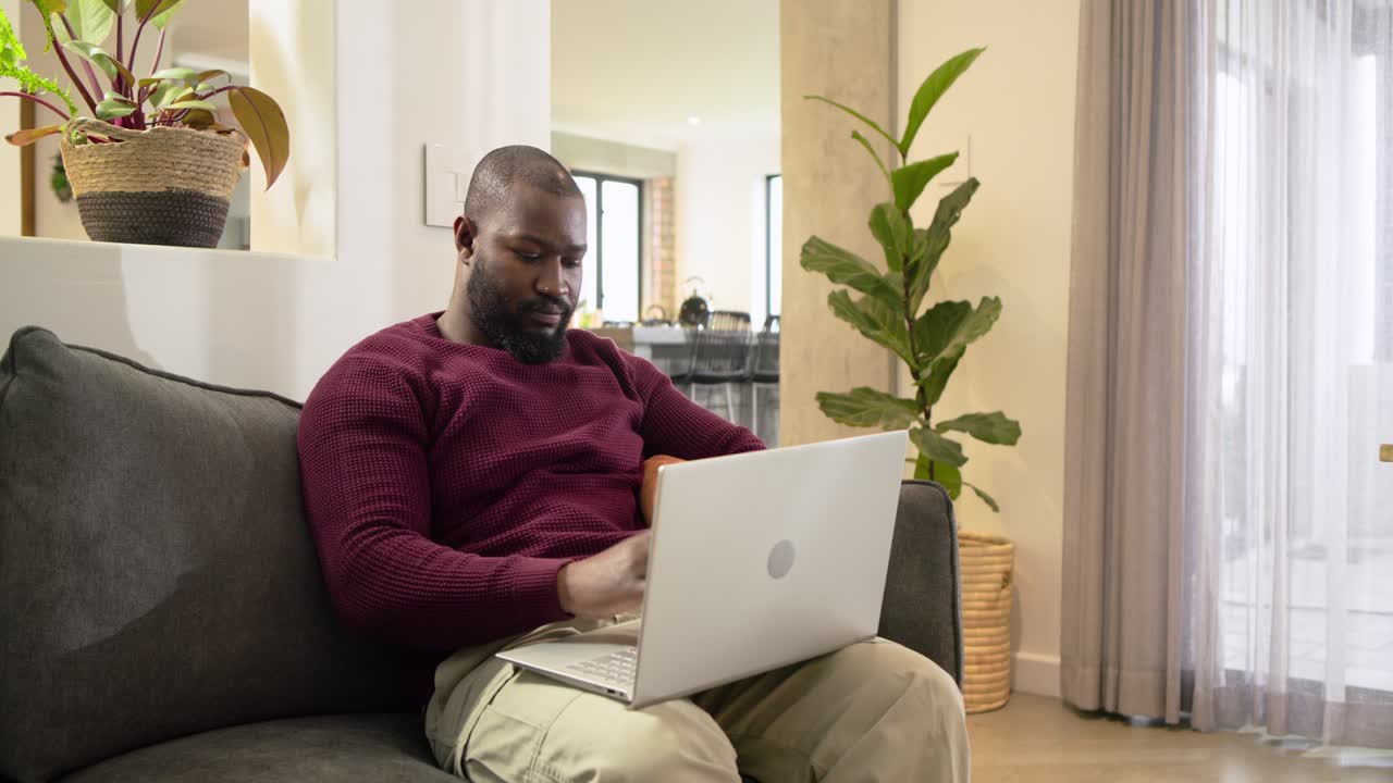 African American man typing on laptop pausing rubbing chest feeling pain resuming typing at home