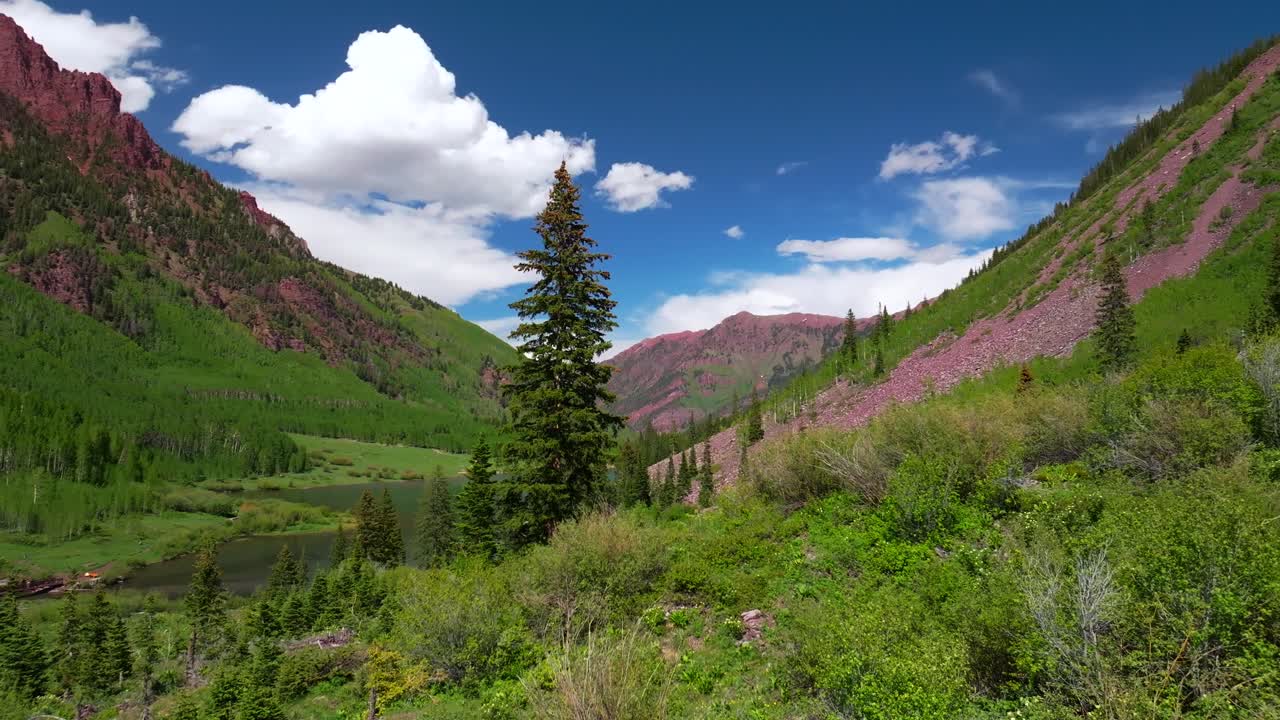 Maroon Lake Crater Lake Aspen Snowmass Maroon Bells Wilderness spring summertime sunny morning blue sky cloud aerial drone Colorado Red steep Rocky Mountains Elk Range Mountains Maroon Creek pan left