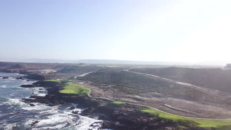 drone flys right to left with large wide views of a beachside golf course and baja's desert landscape