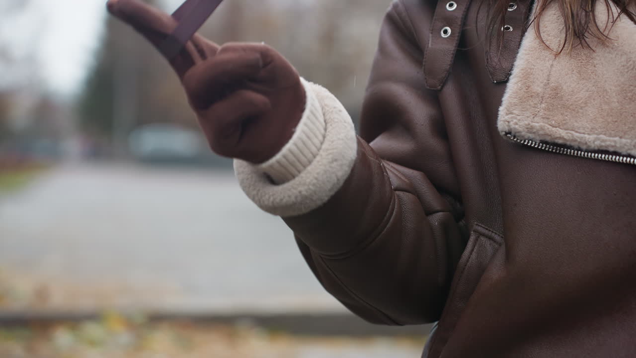 Close view of hand in brown glove and shearling jacket playfully swinging umbrella outdoors during cool autumn day with blurred city background and soft lighting capturing cozy seasonal vibes