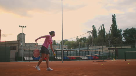 slow motion of woman making tennis serve. slow motion: section of woman bouncing ball on tennis court. athlete serves the tennis ball. young woman is hitting the ball with her tennis racket at sunset