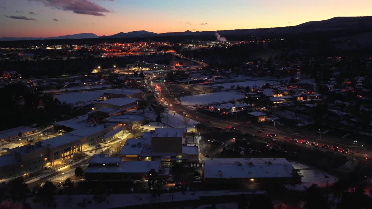 Una veduta aerea dal basso mostra le luci stradali e l'architettura innevata in una città di montagna situata in un canyon. Questa immagine del crepuscolo invernale mostra il quartiere residenziale e le cime distanti durante le festività.