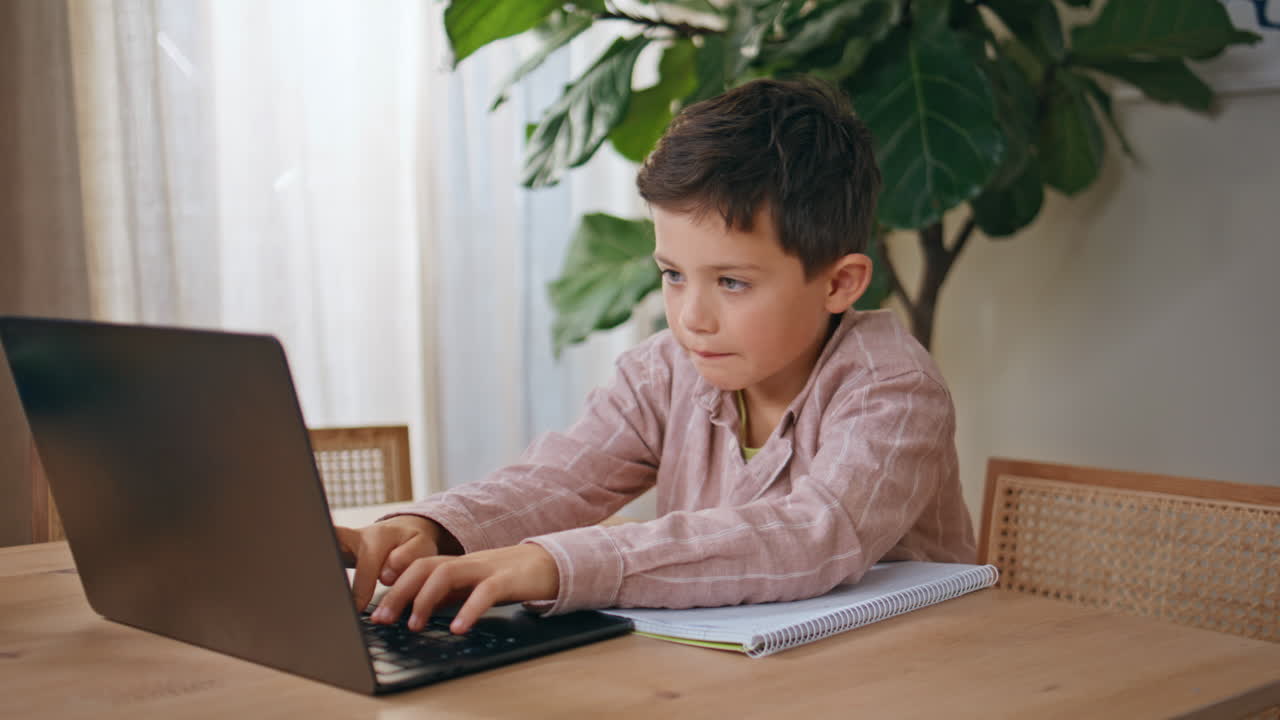 Concentrated child typing laptop studying home closeup. Schoolboy doing homework